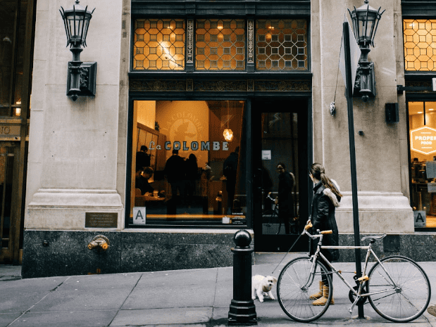 Woman outside a shop holding a bicycle and a leash with a white dog